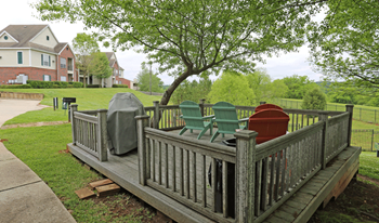 Wood deck with railings on sides, chairs and bbq grill.